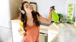 Young woman with headphones on in the kitchen listening to music while cleaning.