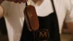 Person in a Magnum apron holding a Magnum Classic ice cream stick freshly dipped in chocolate