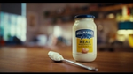 A jar of Hellmann’s mayonnaise with a spoon on a wooden table